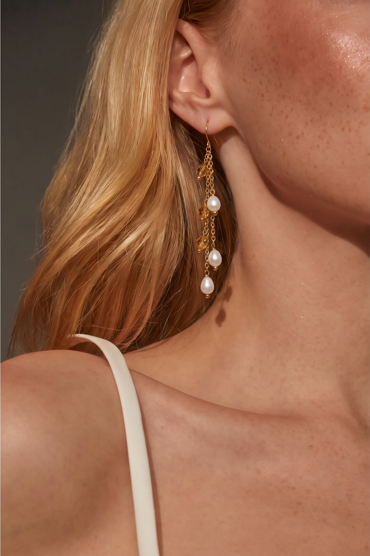 Woman wearing teardrop freshwater pearl and crystal long drop earrings in gold